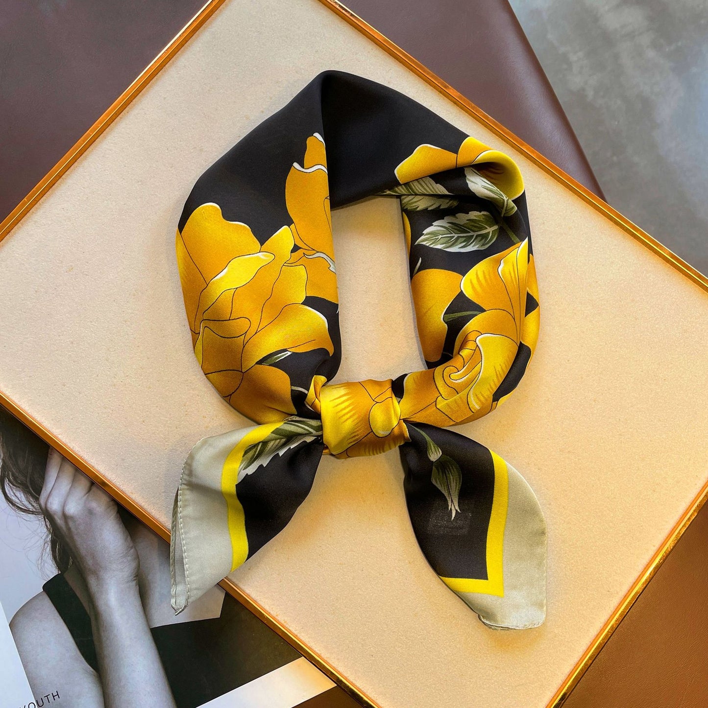 A gauze scarf in yellow with roses, arranged on a table, showcasing its black and yellow floral pattern.