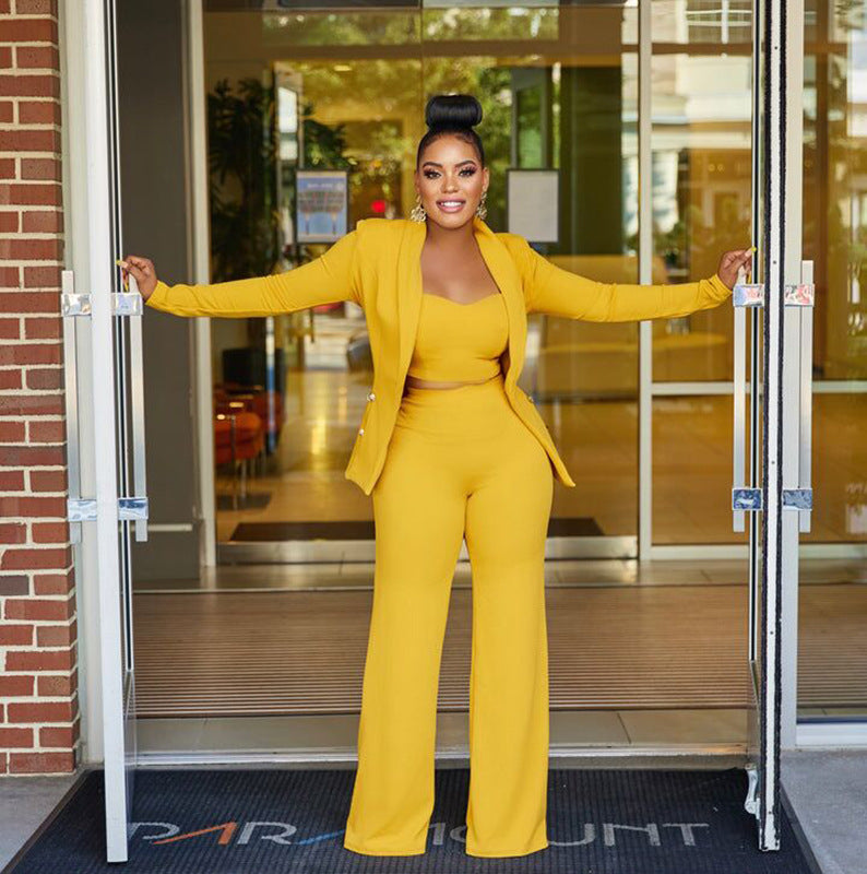 A stylish woman wearing a yellow crop top, pants and blazer and high heels, exuding confidence and elegance.