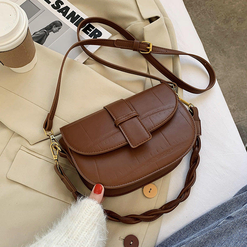 A brown cross body bag resting on a bed.