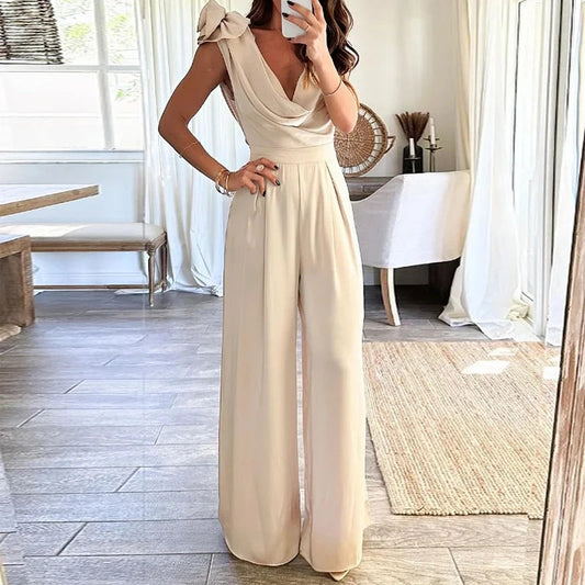 A woman in a beige low collar wide leg jumpsuit capturing a selfie.