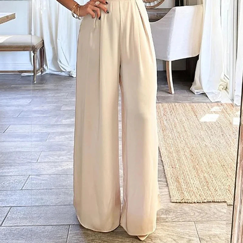 A woman in a beige low collar wide leg jumpsuit capturing a selfie.