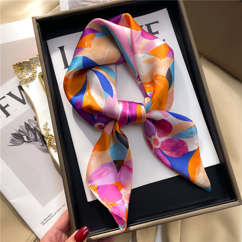 "A woman carefully arranging a box with a beautiful silk gauze scarf, featuring vibrant floral and leaf designs."