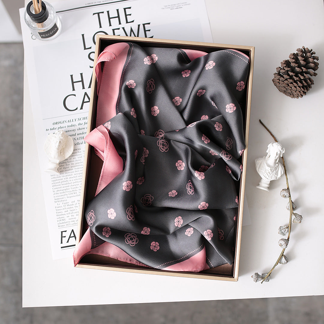 A black and pink scarf with flowers neatly folded in a box, showcasing its Nordic gauze design.