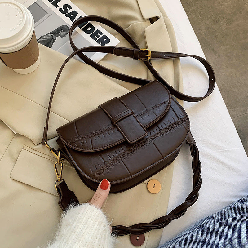 A coffee cross body bag resting on a bed.