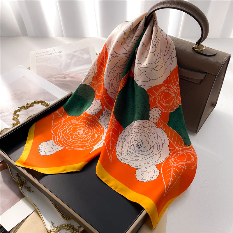 A vibrant orange and green gauze scarf with ranunculi, adding a touch of color to her bag.