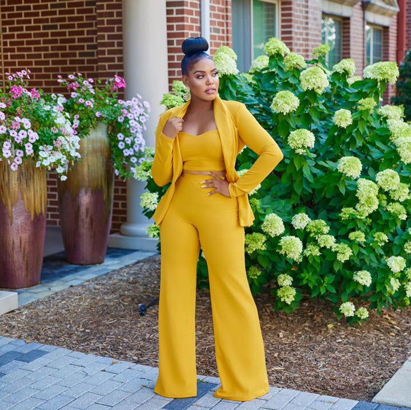 A stylish woman wearing a yellow crop top, pants and blazer and high heels, exuding confidence and elegance.