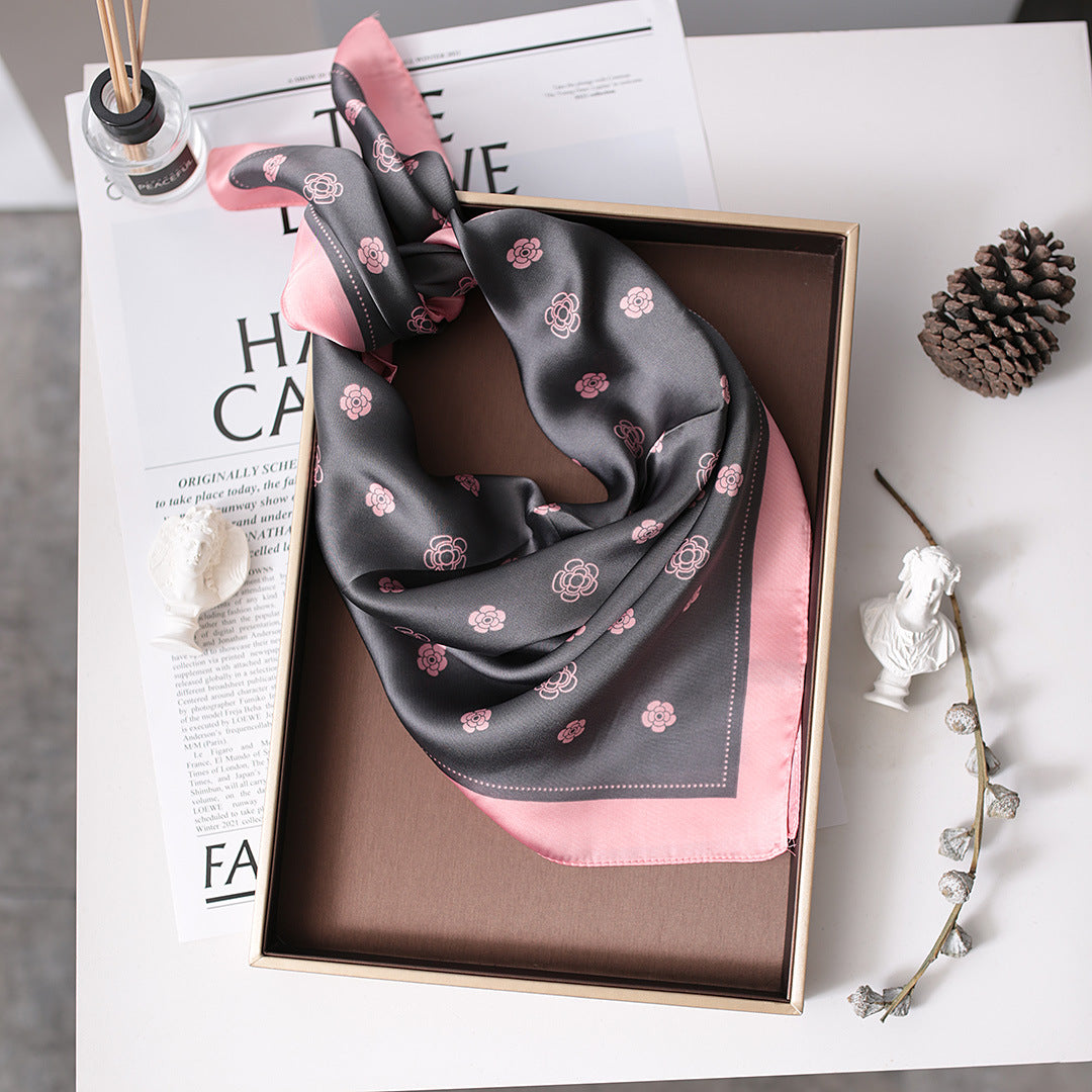 A black and pink scarf with flowers neatly folded in a box, showcasing its Nordic gauze design.