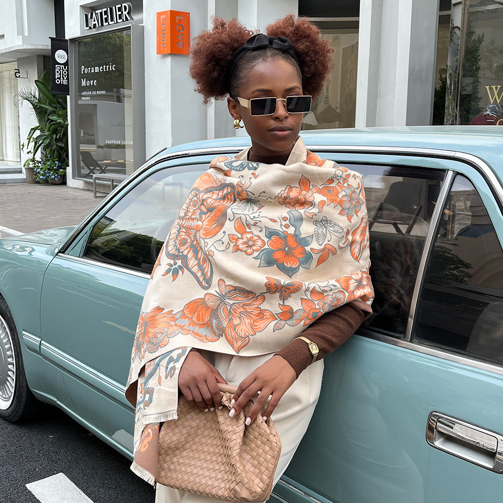 A woman wearing an orange floral print cashmere scarf with butterflies stands gracefully beside a car, exuding elegance and style.