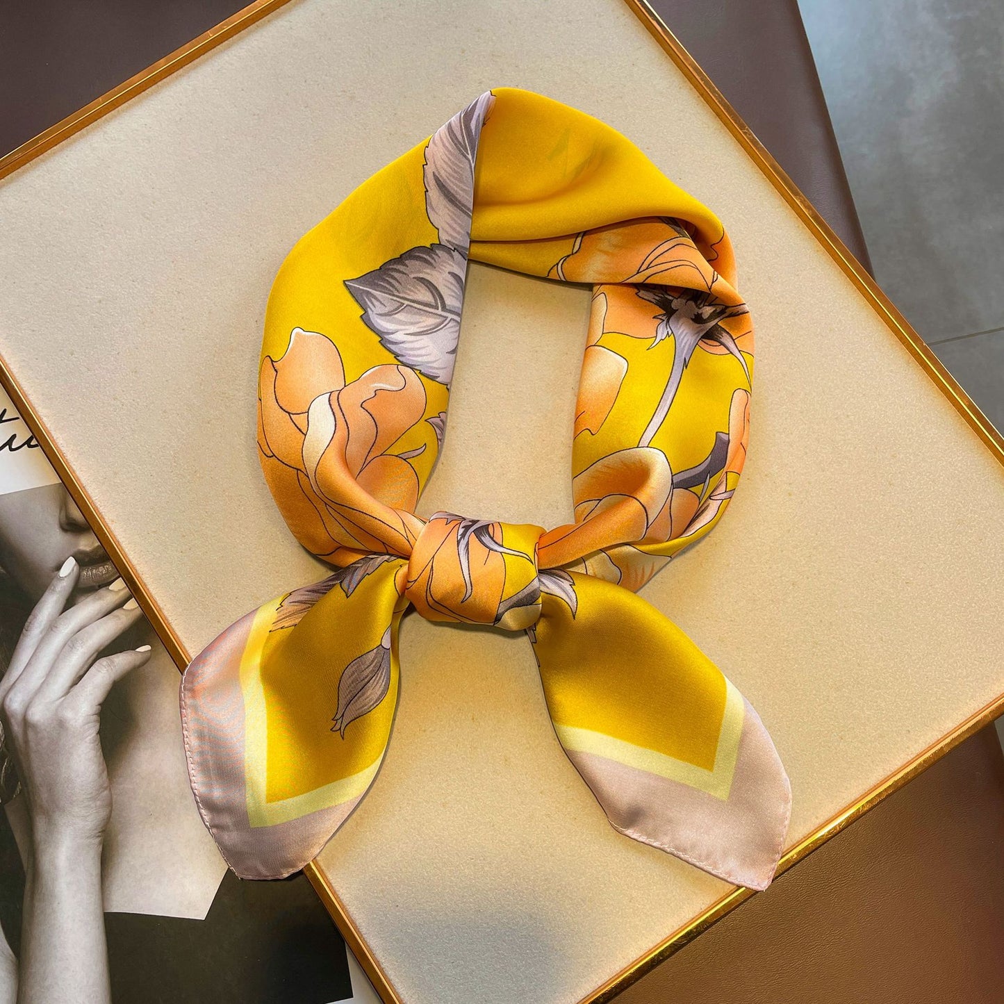 A gauze scarf in yellow with roses, arranged on a table, showcasing its yellow floral pattern.