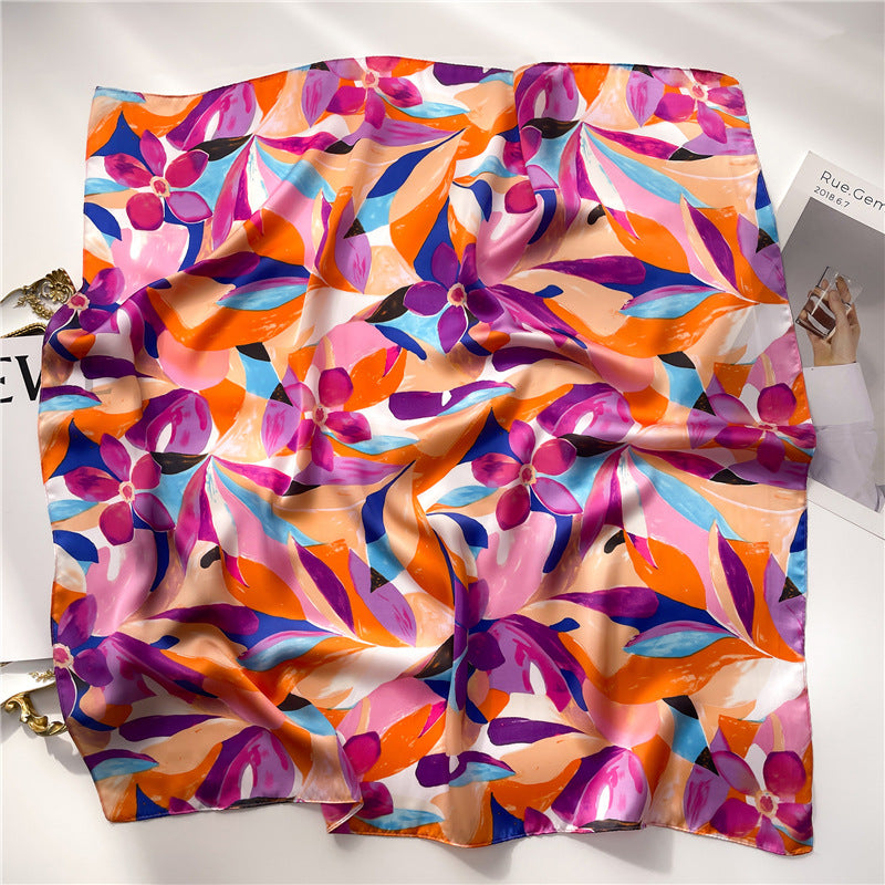 A woman carefully arranging a box with a beautiful purple silk gauze scarf, featuring vibrant floral and leaf designs."