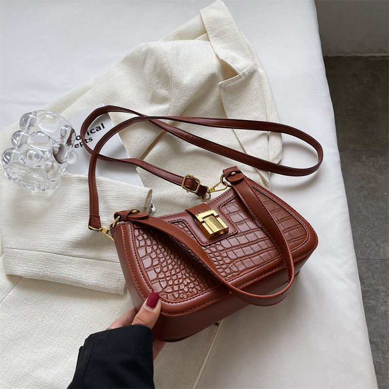 A woman holding a brown crocodile skin bucket bag with gold buckle, showcasing its unique texture and vibrant color.