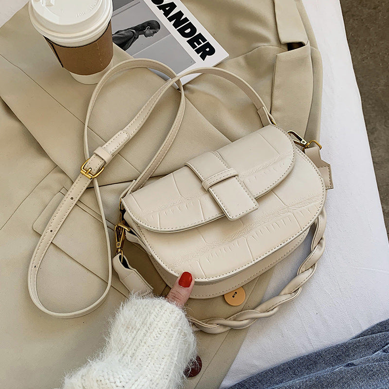 A beige cross body bag resting on a bed.