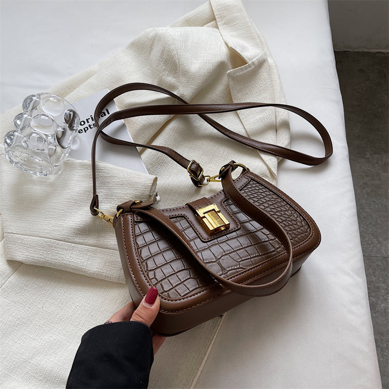 A woman holding a coffee crocodile skin bucket bag with gold buckle, showcasing its unique texture and vibrant color.