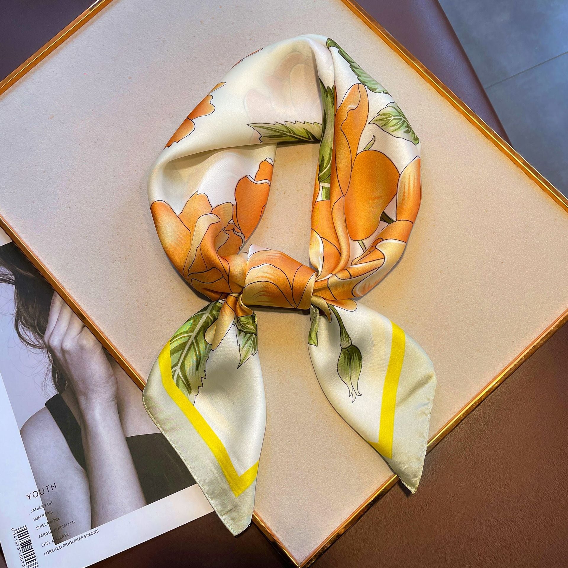 A gauze scarf in yellow with roses, arranged on a table, showcasing its white and yellow floral pattern.