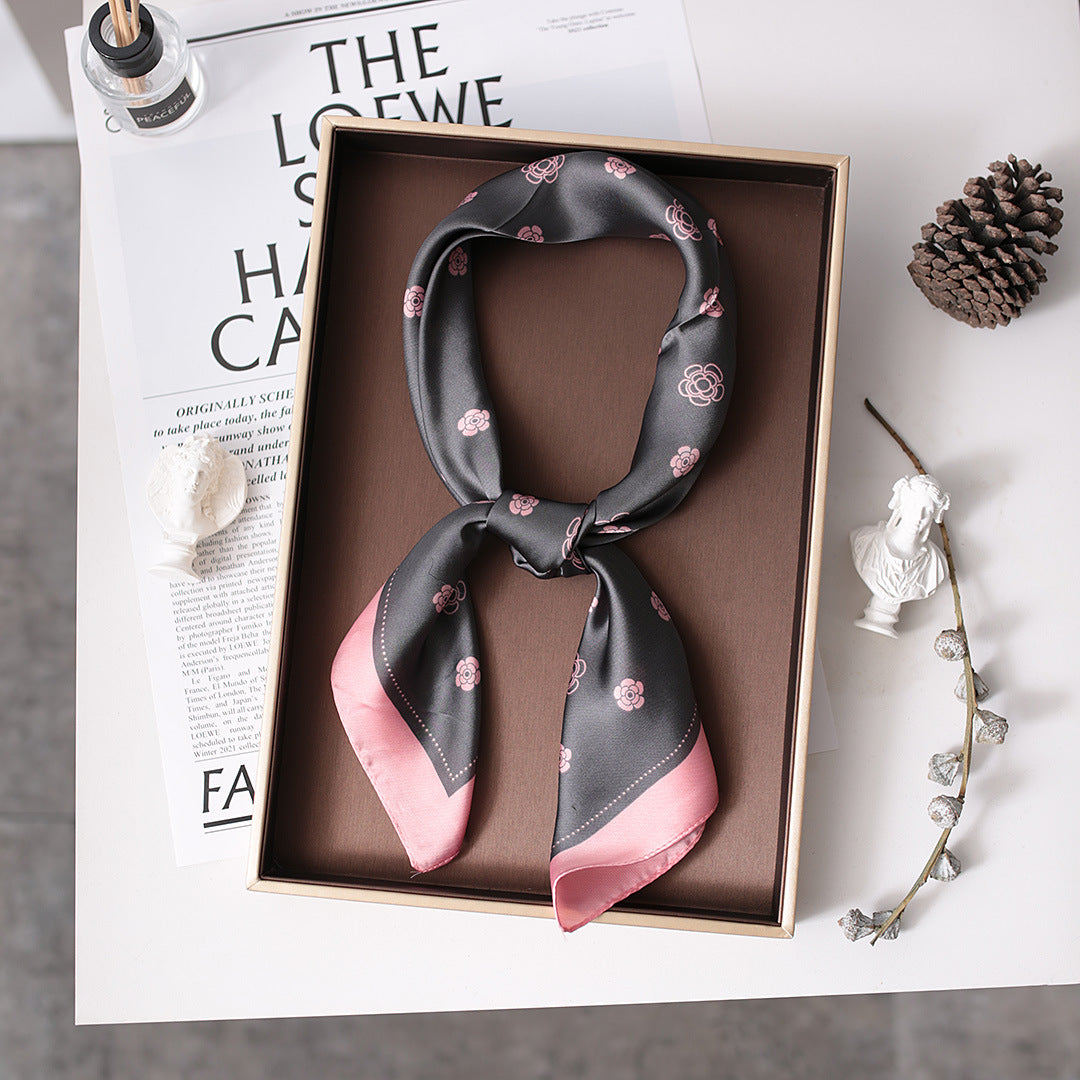 A black and pink scarf with flowers neatly folded in a box, showcasing its Nordic gauze design.