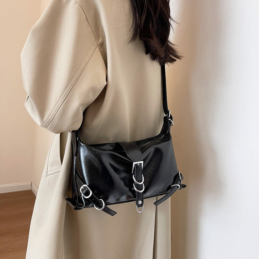 A woman in a trench coat holding a metallic-like black bag with a silver buckle.