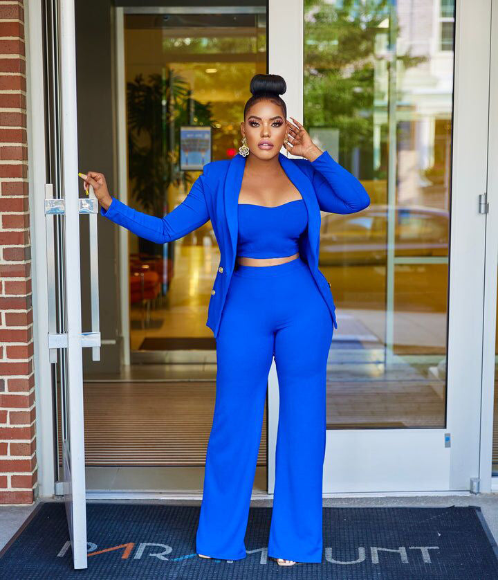 A stylish woman wearing a blue crop top, pants and blazer and high heels, exuding confidence and elegance.