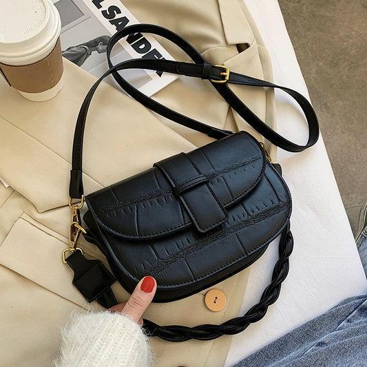 A black cross body bag resting on a bed.